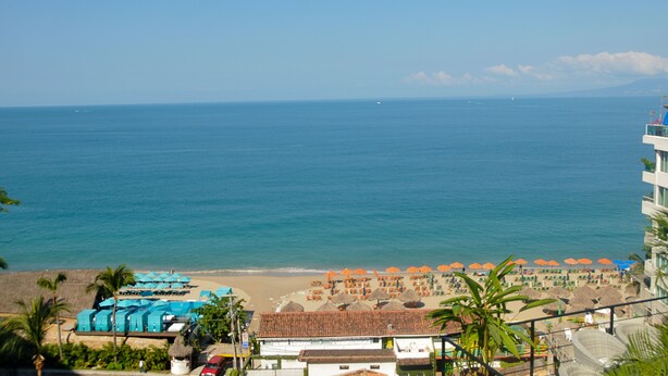 Vista de la playa con un hotel, sombrillas y cielo despejado.