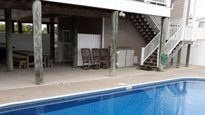 A swimming pool with a wooden deck area, a covered seating area, and a staircase leading to an upper level.