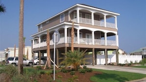A two-story beachfront house with a balcony, surrounded by palm trees and a well-maintained lawn.