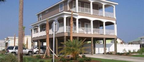 A two-story beachfront house with a balcony, surrounded by palm trees and a well-maintained lawn.