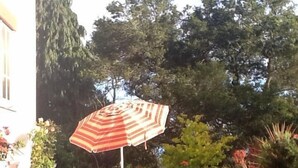 Een terras van stenen met een gestreept zonnescherm, een tafel en stoelen.