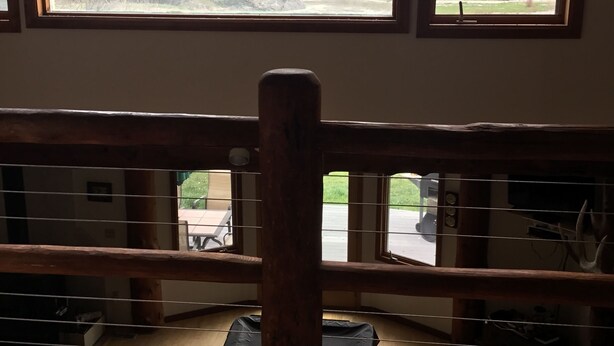 A room with a wooden floor, a large window with a view of a mountainous landscape, and a wooden railing. - Life is Good Lodge Montana on Gary Cooper Ranch at Dearborn River (Cascade)