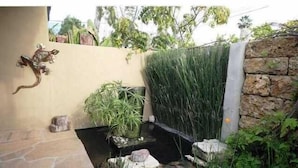 Un jardín con un muro de piedra, un estanque pequeño y diversas plantas.