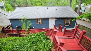 Une maison bleue avec une terrasse rouge et un toit en métal, entourée de verdure.