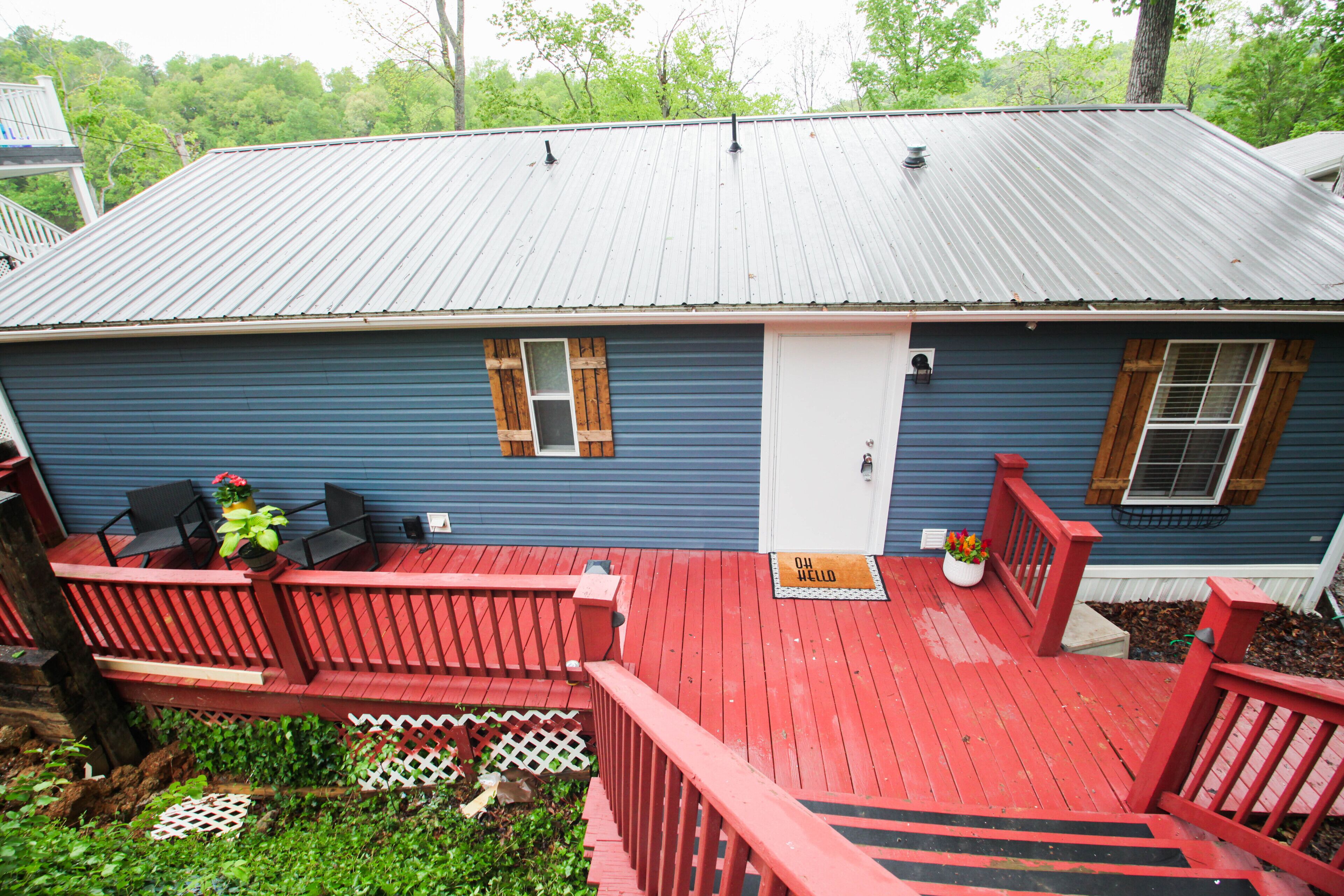 A blue house with a red deck, a white garage door, and a small porch with a bench and potted plants.