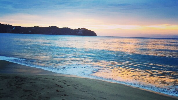 A beach with footprints leading to the water, a calm sea, and a distant landmass under a clear sky. - Best Location in Sayulita.Stunning Ocean Views. 2 min walk to beach (Sayulita)