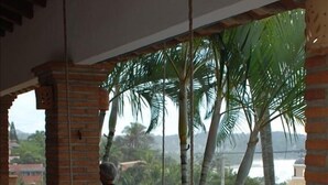 A room with a bed, a table, and chairs. There is a view of palm trees and a body of water outside. - Best Location in Sayulita.Stunning Ocean Views. 2 min walk to beach (Sayulita)