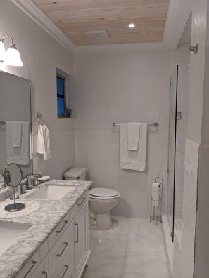 Un baño moderno con lavamanos de mármol, inodoro y cabina de ducha con paredes de vidrio.