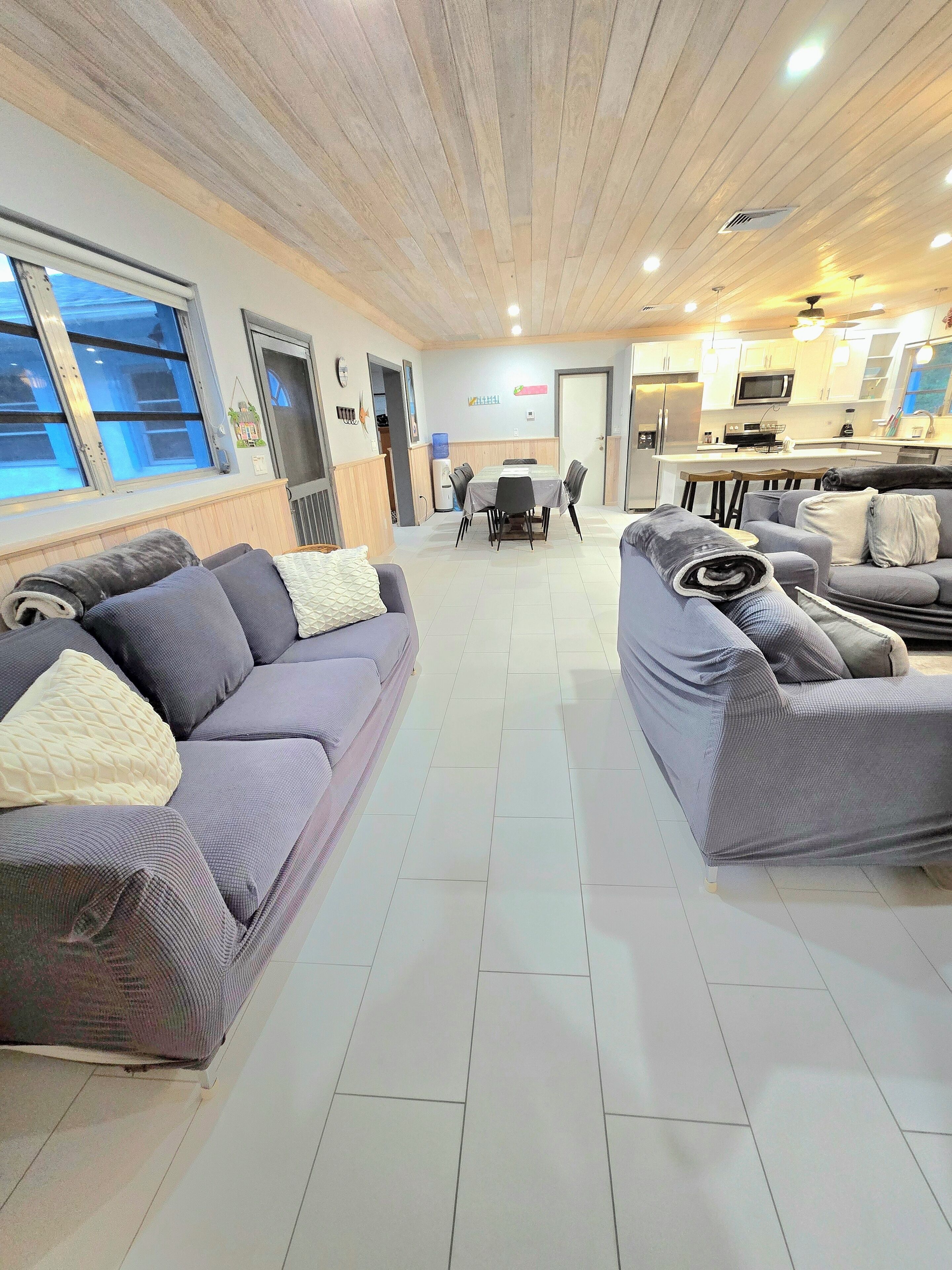 A modern living room with two grey sofas, a dining table, and a kitchen area in the background.