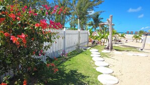 Un jardín con cerca blanca, piedras para pisar y plantas tropicales.