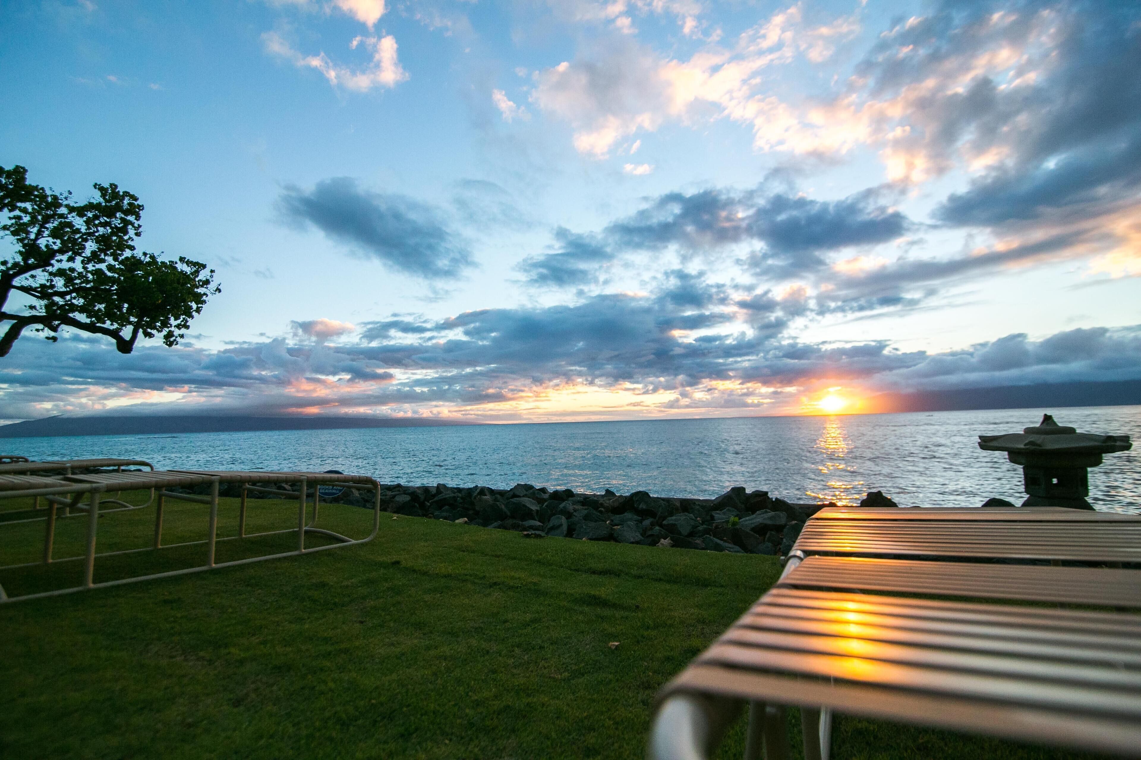 Vista del atardecer sobre una masa de agua, con una mesa de picnic y un farol de piedra al frente.