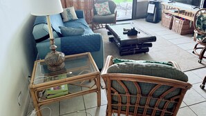 A living room with a sofa, a coffee table, a chair, a TV, and a view of the ocean.
