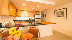 A modern kitchen with wooden cabinets, a stainless steel refrigerator, and a dining area with a glass table and chairs.