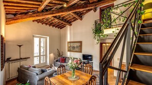 Un salon chaleureux avec une table à manger en bois, un canapé gris et un escalier doté d’une rampe en métal.