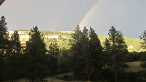 Eine Landschaft mit Regenbogen, Bäumen und einem Gebäude in der Ferne.