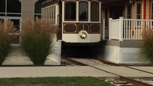 Un petit wagon de train à l’extérieur blanc et marron, avec un toit noir et une rambarde blanche sur le côté.