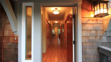 A hallway with wooden floors and doors, leading to a room with a fireplace and a hanging lantern.