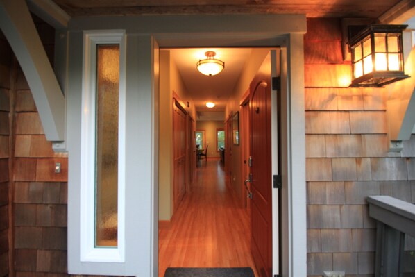 A hallway with wooden floors and doors, leading to a room with a fireplace and a hanging lantern.