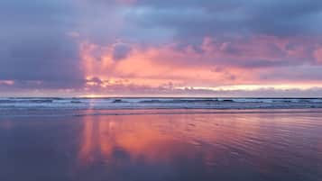 A beach with a sunset, calm waves, and a clear sky.