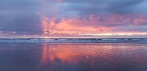 A beach with a sunset, calm waves, and a clear sky.