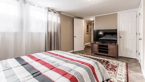 A bedroom with a bed, a TV, and a door leading to another room.