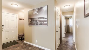 A hallway with beige walls, a large framed picture of a beach scene, and a door with a coat rack beside it.