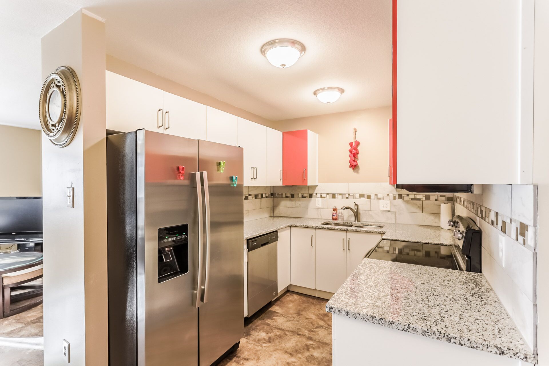 A modern kitchen with stainless steel appliances, white cabinets, a granite countertop, and a red accent wall.