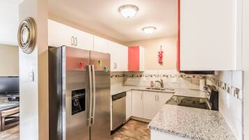 A modern kitchen with stainless steel appliances, white cabinets, a granite countertop, and a red accent wall.