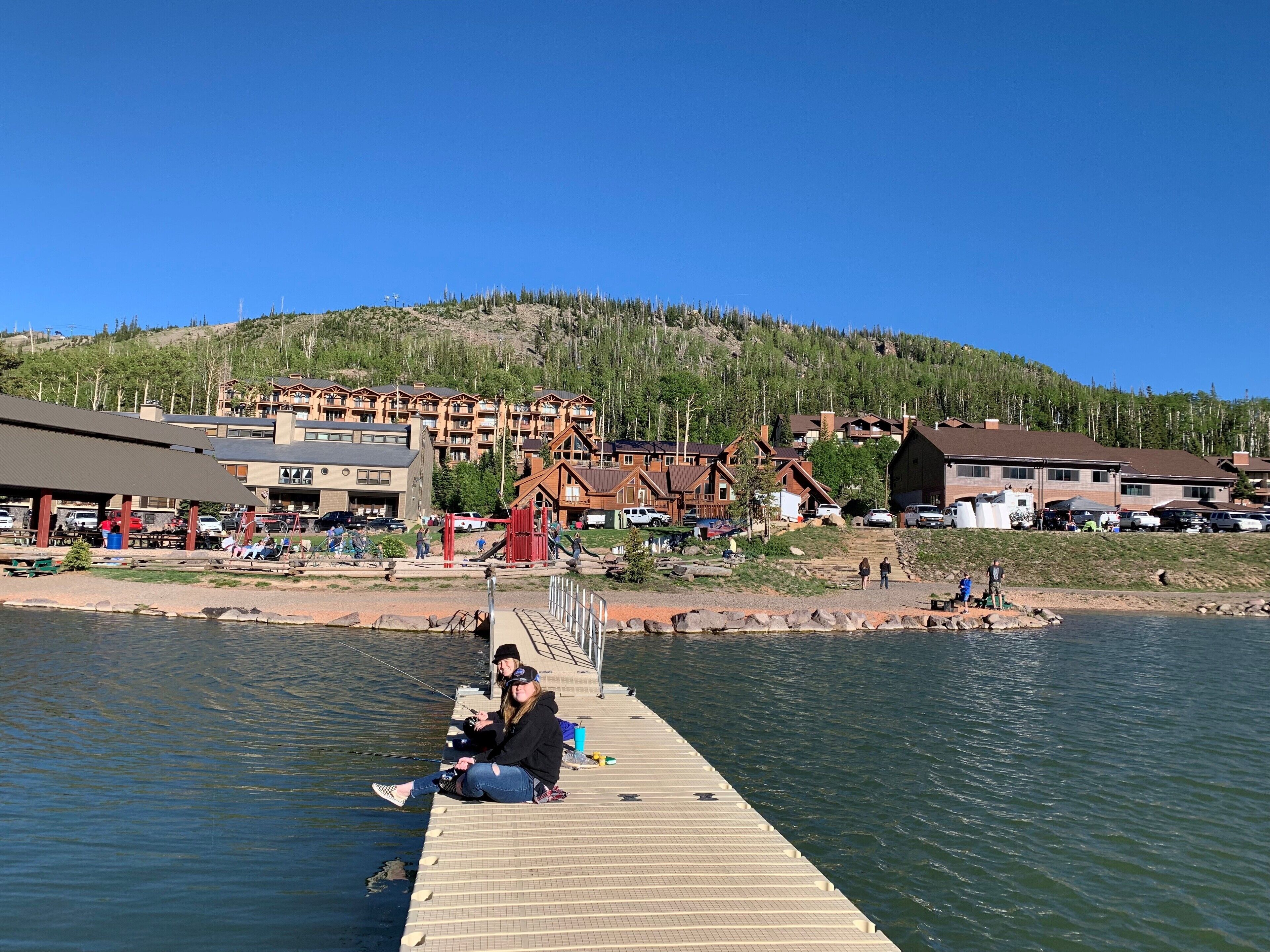 Une jetée s’avançant dans un lac, avec en arrière-plan un ensemble de bâtiments d’un chalet et une colline boisée.