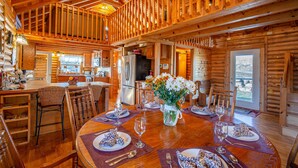 A wooden cabin interior with a dining area, kitchen, and a large window.