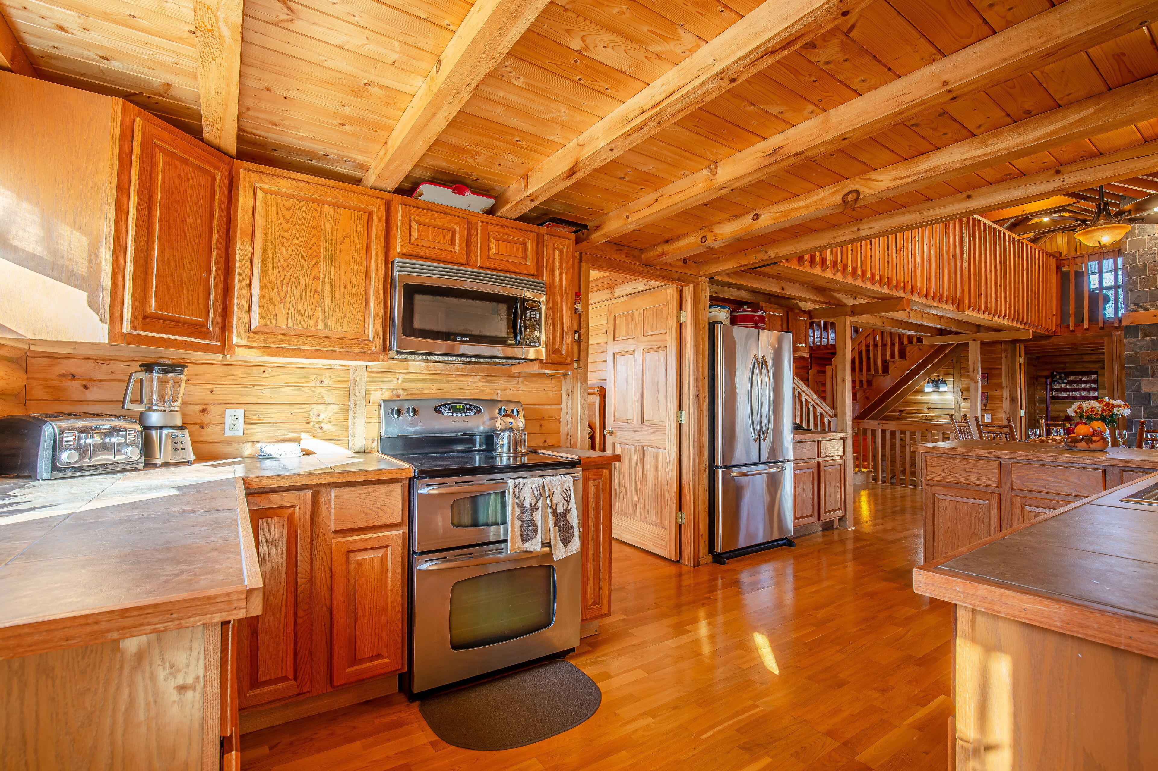 A wooden cabin interior with a kitchen featuring a microwave, toaster, stove, and refrigerator.
