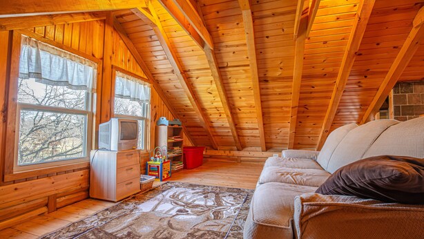 A cozy attic room with wooden beams, a sofa, a television, and a window with curtains.