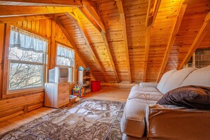 Um quarto de sótão acolhedor, com vigas de madeira, um sofá, uma televisão e uma janela com cortinas.