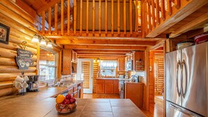 A log cabin kitchen with wooden walls, a stainless steel refrigerator, and a fruit bowl on the counter.