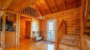 A log cabin interior with a wooden staircase, a bench, and a door leading outside.