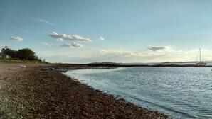 Ein Strand mit felsiger Küste, eine Segelyacht auf dem Wasser und eine entfernte Landmasse.