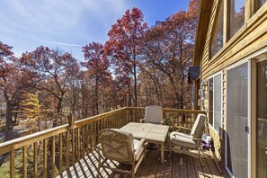 Une terrasse en bois avec une table et des chaises, donnant sur une forêt aux couleurs automnales.