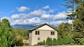 A single-story house with a front porch, surrounded by trees and a mountain backdrop.
