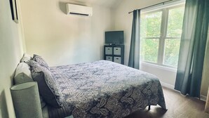 A bedroom with a bed, a bedside table with a lamp, a TV, and an air conditioning unit.