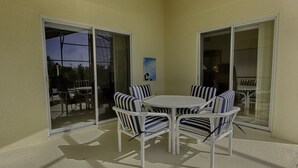 Eine Terrasse mit einem runden Tisch und sechs gestreiften Stühlen, umgeben von Glastüren.