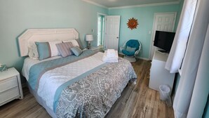 A bedroom with a bed, a chair, a television, and a ceiling fan.