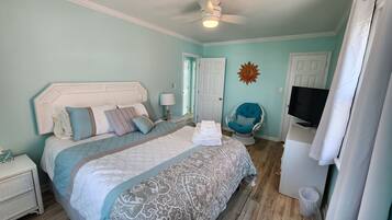 Une chambre à coucher avec un lit, une chaise, un téléviseur et un ventilateur de plafond.