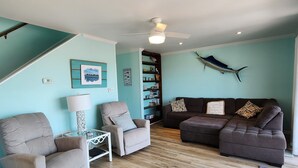 A living room with teal walls, a ceiling fan, a bookshelf, and a dark brown sofa.
