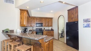 A kitchen with wooden cabinets, a granite countertop, a black refrigerator, and a microwave.