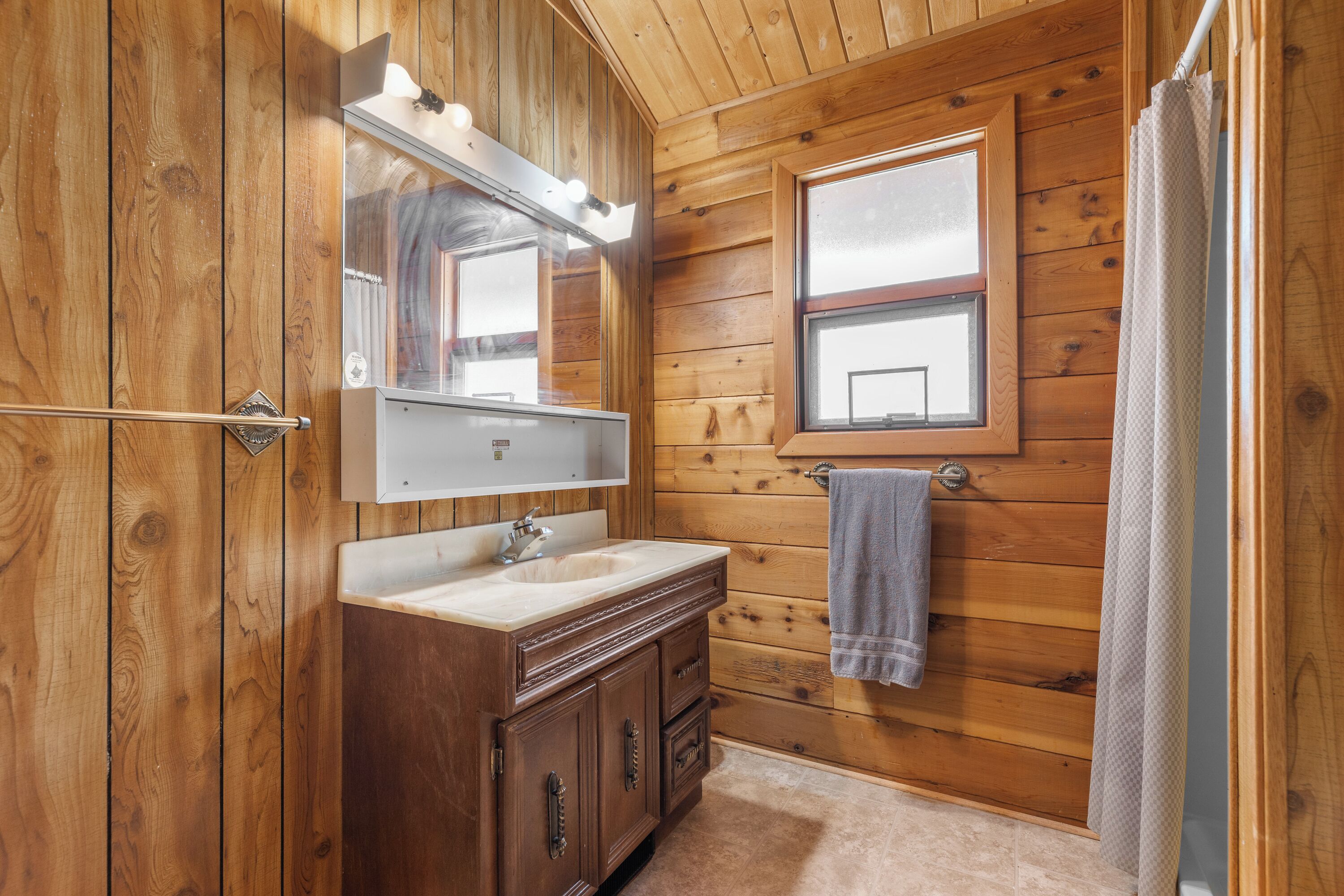 Un baño con paneles de madera, tocador, espejo y ventana.