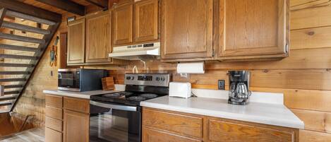 A wooden cabin kitchen with a stove, microwave, and cabinets.