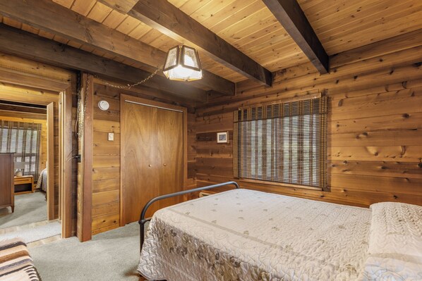 Una habitación tipo cabaña de madera con una cama, una puerta y una ventana con persianas.