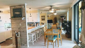 Una cocina moderna con armarios blancos, un muro decorativo de madera y una zona de comedor con sillas y mesa de madera.