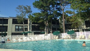 Zona de piscina con sillas de descanso y sombrillas, rodeada de edificios de varios pisos con balcones.