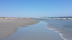A wide beach with gentle waves, a pier in the distance, and people enjoying the seaside.